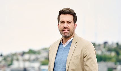 Aaron Posey, a man in a tan jacket standing in front of a city.