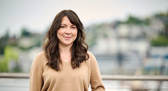 Evan Delay, a woman in a tan sweater is posing for a photo with the Bloodworks Bio logo displayed prominently.