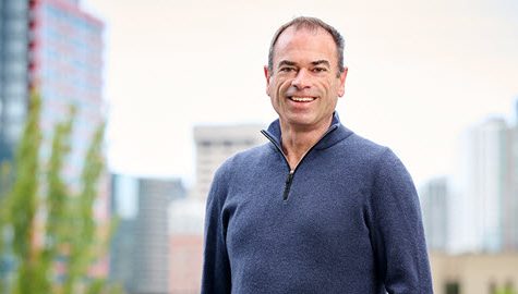 Tim Waters, a man in a blue sweater, standing in front of a city.